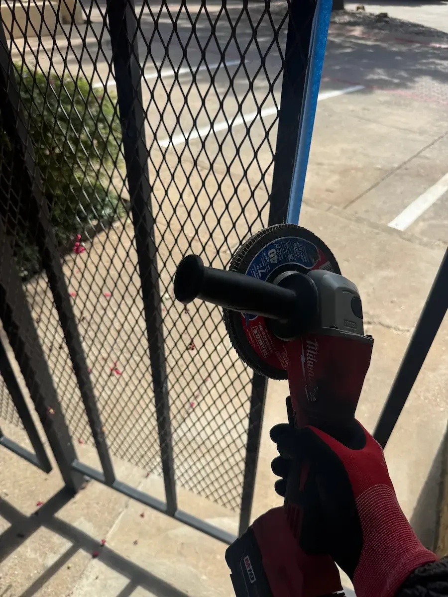 Installer trimming a black ornamental metal fence panel with an angle grinder