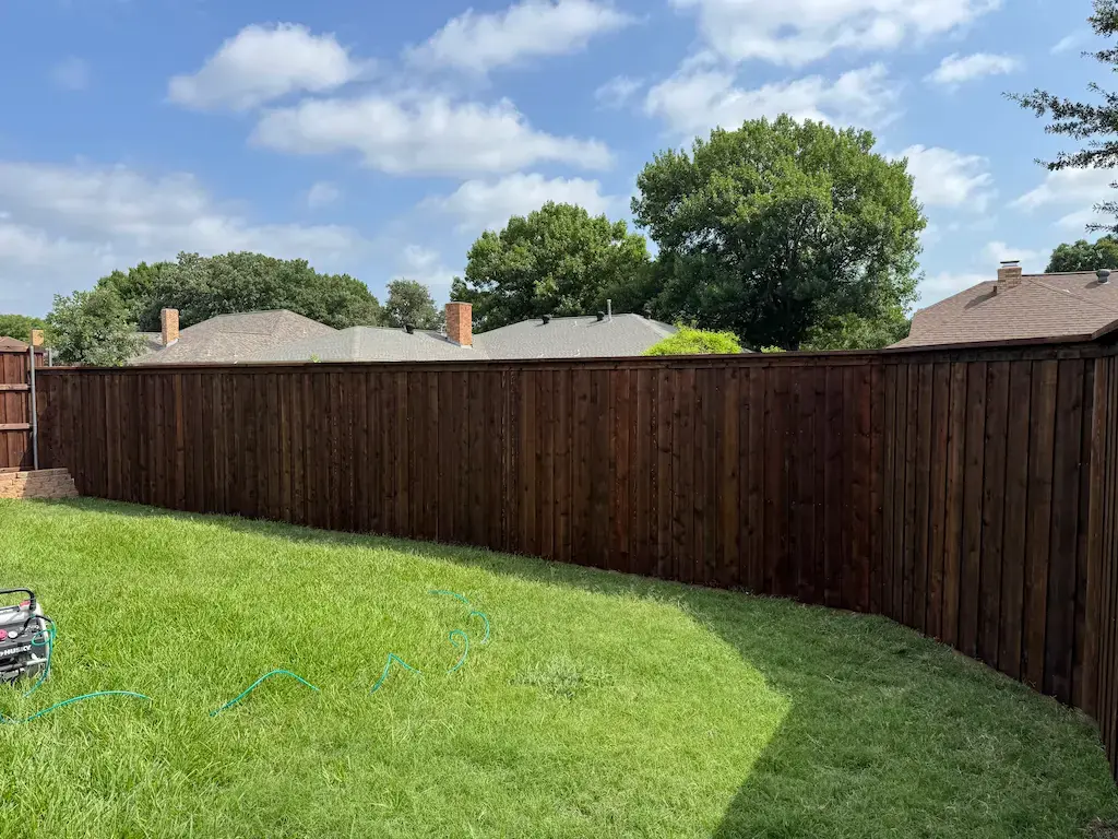 Dark-stained wood privacy fence curving around a green backyard under a blue sky